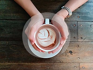 Female hands holding cup of chocolate on wooden background. top view.