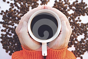 Female hands holding a cup of coffee with coffee beans on white background.