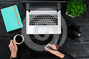 Female hands holding a cup of coffee and typing on the keyboard of a laptop on black wooden table.