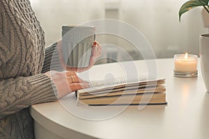 Female hands holding cup of tea or coffee in front of opened book. Cozy Mood Home Concept