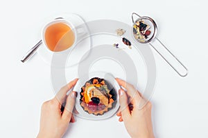 Female hands holding dessert cake next to cup of fresh tea