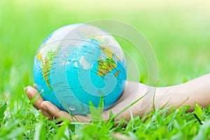 Female hands holding floating earth on natural green background.