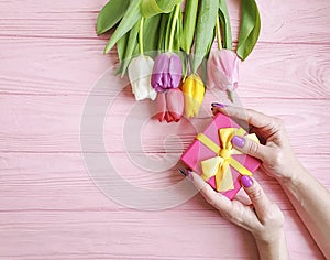 Female hands holding a gift box spring   present birthday , romantic  a bouquet of tulips on a wooden background