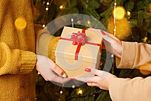 Female hands holding gift box near Christmas tree with lights. New year is coming