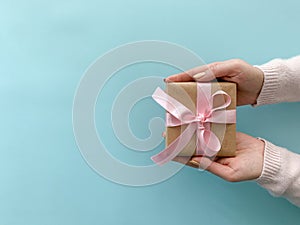 Female hands holding gift box with pastel pink ribbon on soft blue color background