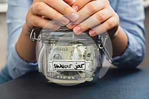 Female hands holding Glass jar full of American currency dollars cash banknote with text SWEAR JAR. Preparation saving