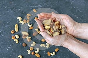 Female hands holding handful of almonds nuts on dark background. Cashew, hazelnuts,  and Brazil nuts top view. Healthy vegetarian