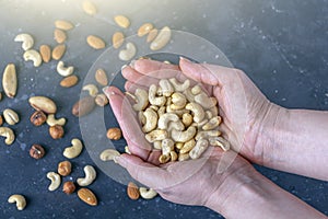 Female hands holding handful of almonds nuts on dark background. Cashew, hazelnuts,  and Brazil nuts top view. Healthy vegetarian