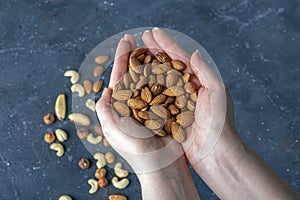 Female hands holding handful of almonds nuts on dark background. Cashew, hazelnuts,  and Brazil nuts top view. Healthy vegetarian