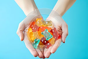 Female hands holding a handful of Multi-colored cbd gummy bears on a blue background. View from above