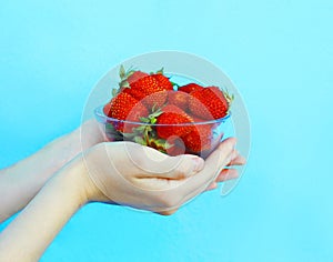 Female hands holding handful of strawberries close up over blue