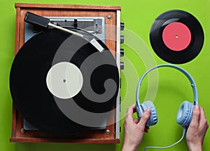 Female hands holding headphones against the background of retro vinyl record player with vinyl records on green background.