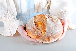 Female hands holding homemade crusty loave of bread. Cooking of healthy wheat bread. Fermented food