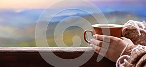 Female hands holding hot cup of coffee or tea on the mountains background.