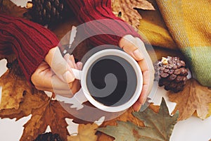 Female hands holding hot dark coffee, blanket and autumn leaves on white background.