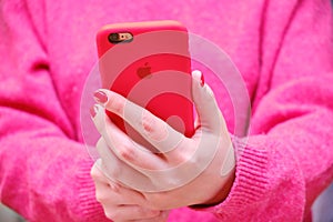 Female hands holding the iphone Apple in a red case. The girl holds the phone and takes a selfie photo