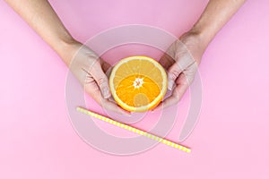 Female hands holding juicy orange half with a yellow straw in front of it