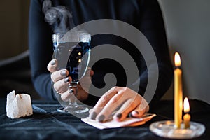 Female hands holding magic love potion and occultic fortune-telling cards on dark background