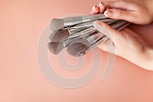 Female hands holding makeup brushes for powder or eyeshadow on coral colored background.