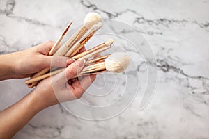 Female hands holding makeup brushes for powder or eyeshadow on coral colored background.