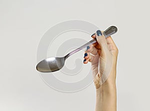 Female hands holding a metal tablespoon. Isolated on gray background. Closeup