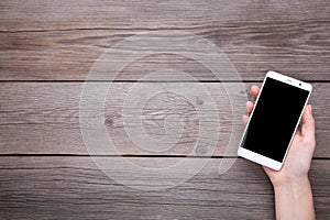 Female hands holding mobile phone with blank screen on grey wood background. Smartphone on wood table