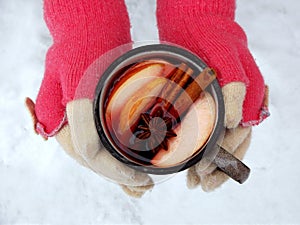 Female hands holding mug of mulled wine with apple and spices. Cup of seasonal hot drink. Homemade fruit tea.