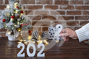 Female hands holding the number 2 to complete the new year 2022. Merry Christmas, small Christmas tree on wooden table with red