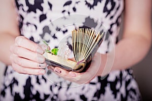 Female hands holding old book and pink carnation flower on a black white background