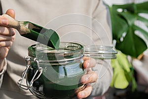 Female hands holding Organic blue-green algae spirulina detox powder in glass jar. Health protein of chlorella. Vitamins
