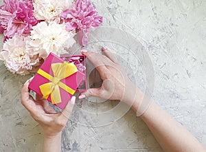 Female hands holding a peony flower gift box on a gray concrete background