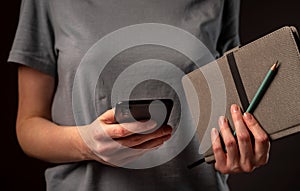 Female hands holding phone and making appointments, holding planner. Student using smartphone and notebook at night