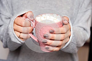 Female hands holding pink cup of coffee with marshmallow