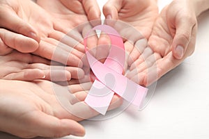 Female hands holding pink ribbon on light background, closeup. Breast cancer awareness concept