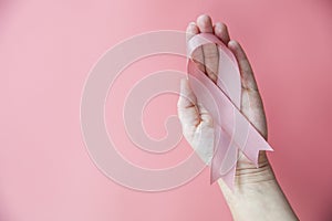 Female hands holding pink ribbon over pink background, breast cancer awareness, October pink concept top view with copy