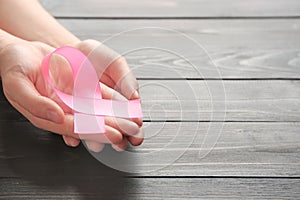 Female hands holding pink ribbon on wooden background. Breast cancer awareness concept
