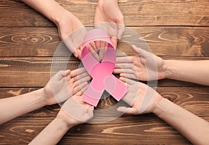 Female hands holding pink ribbon on wooden background. Breast cancer awareness concept