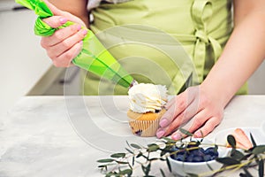 Female hands holding piping bag filled with cream cheese and decorating cupcakes. Pastry chef using a pastry bag