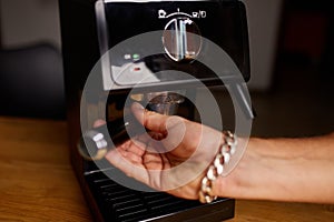 Male barista hand making espresso from ground coffee maker at modern cafe