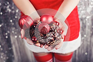 Female hands holding red Christmas decorations and cones, shiny xmas background. Holiday gift and ornaments. Toning