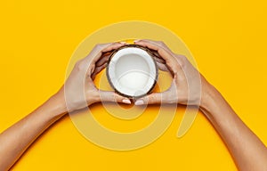 Female hands holding ripe coconut on yellow colored background, minimal flat lay style top view with copy space. Pop art design, c