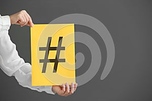 Female hands holding sheet of paper with hashtag sign on grey background