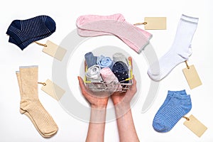 Female hands holding shopping basket with socks among women`s cotton socks set with price tags on white background. Fashionable