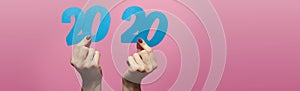 Female hands holding and showing date 2020 cut out of cardboard on a colored pink background, concept new year,creative idea