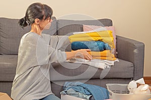 Female hands holding stack of bed linen. Woman preparing items and packing into cardboard box. Donations for charity