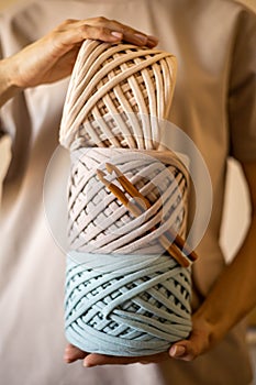 Female hands holding stack of hank reels multicolored ribbon yarn and wooden crochet needle