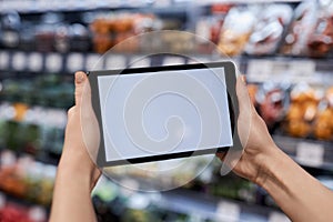 Female hands holding tablet with white screen mockup in supermarket
