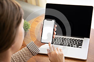 Female hands holding touch phone with isolated screen above the table with laptop in the office