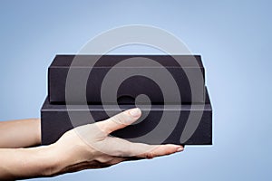 Female hands holding two elegant black cardboard boxes on light blue background. Present, shopping, free shipping