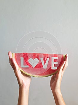 female hands holding up slice of watermelon with word love